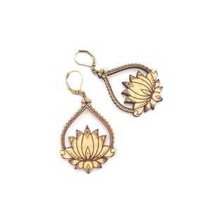 May include: A pair of wooden earrings with a lotus flower design. The earrings are a light brown color and have a gold-colored hook.