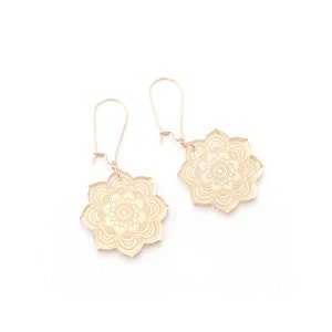 May include: A pair of gold-toned earrings with a delicate mandala design. The earrings are made of metal and have a simple, elegant style.