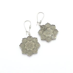May include: A pair of silver earrings with a gray mandala design. The earrings are made of metal and have a hook closure.