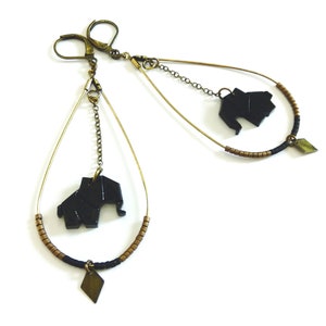 Puede incluir: Un par de pendientes colgantes con dijes de elefante de origami negro y cadenas doradas. Cada pendiente presenta una gota de cuentas negras y doradas con un dije de diamante dorado.