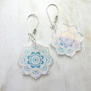 May include: A pair of iridescent silver earrings with a white and blue mandala design.