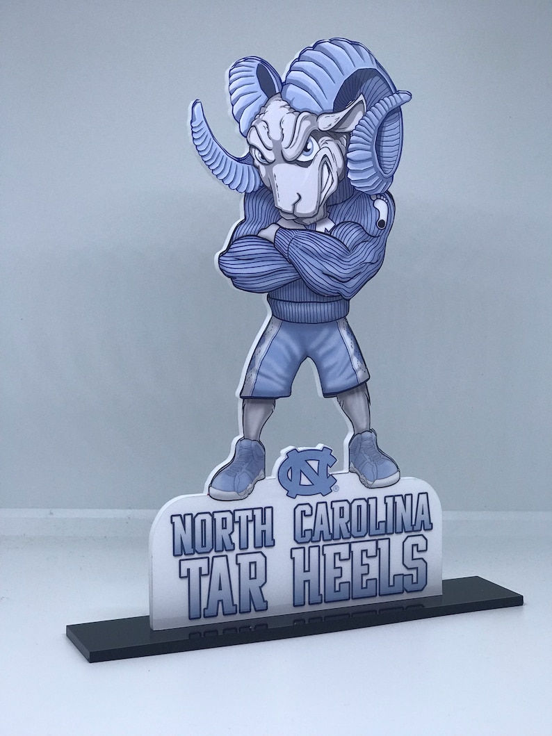 May include: A blue and white 3D cutout of the North Carolina Tar Heels mascot, a ram with a blue sweater and shorts, standing on a black base. The base has the words "North Carolina Tar Heels" printed on it.