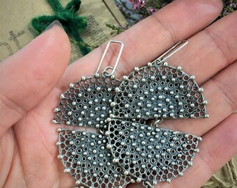 Può includere: Un paio di orecchini d'argento con un design delicato e intricato. Ogni orecchino presenta una forma circolare con un motivo a taglio e un piccolo ciondolo pendente.