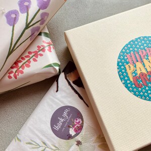 Pode incluir: Tr&ecirc;s presentes embrulhados com papel estampado floral. Uma caixa de presente tem um adesivo que diz "Obrigado pelo seu neg&oacute;cio!" Outra caixa de presente tem um adesivo que diz "Hippie Panda Crafts Etsy".