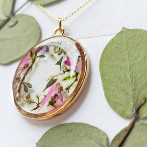 May include: A gold necklace with a round pendant featuring pressed flowers and leaves encased in clear resin.