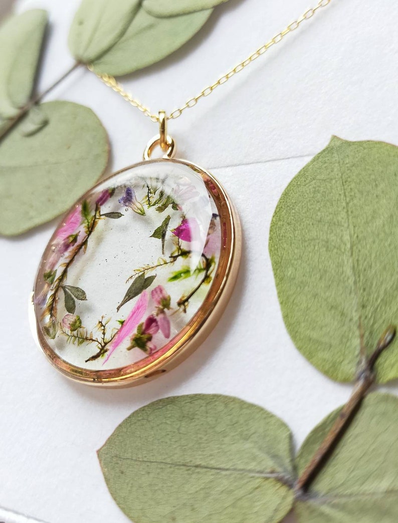 May include: A gold necklace with a round pendant featuring pressed flowers and leaves encased in clear resin.