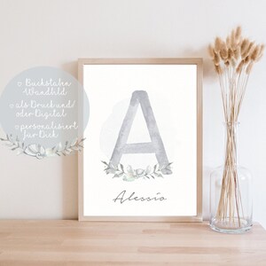 Puede incluir: Una impresi&oacute;n de acuarela de la letra A en gris con una corona de flores alrededor. El nombre Alessio est&aacute; escrito debajo de la letra. La impresi&oacute;n est&aacute; enmarcada y se muestra en una superficie de madera.