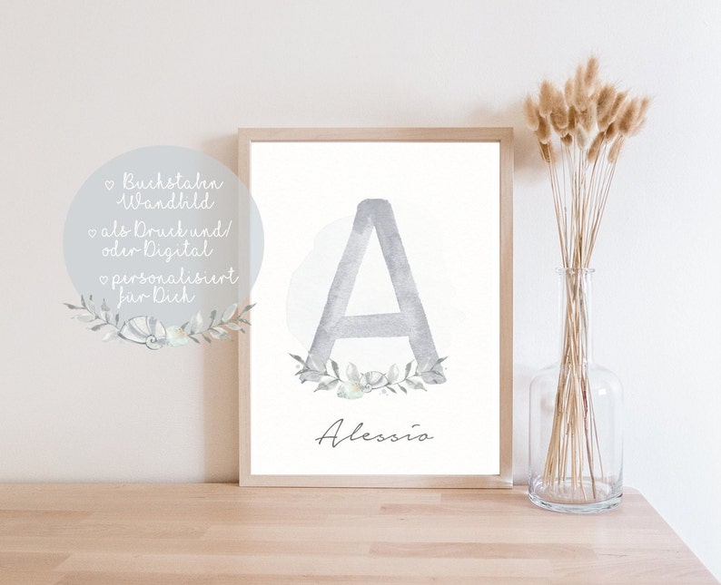 Puede incluir: Una impresi&oacute;n de acuarela de la letra A en gris con una corona de flores alrededor. El nombre Alessio est&aacute; escrito debajo de la letra. La impresi&oacute;n est&aacute; enmarcada y se muestra en una superficie de madera.