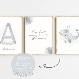 Puede incluir: Tres impresiones de acuarela en tonos azul claro y gris. La primera impresi&oacute;n presenta la letra A con una corona floral y el nombre Alessio. La segunda impresi&oacute;n tiene el texto "Du bist unser kleines Wunder". La tercera impresi&oacute;n muestra una ballena con una corona floral.