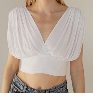 May include: A white crop top with a V-neck and puffed sleeves. The top is made of a soft, lightweight fabric and has a fitted bodice.
