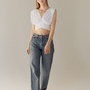 May include: A woman wearing a white crop top with a V-neck and a pair of blue denim jeans.