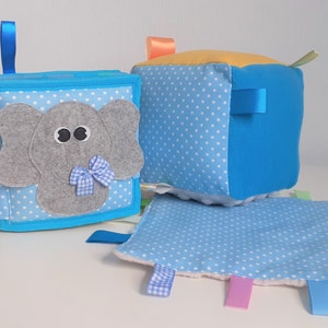 Può includere: Un giocattolo per bambini in tessuto blu e bianco con un viso di elefante, un fiocco a scacchi blu e bianco e un nastro blu. Il giocattolo è fatto di tessuto morbido e ha una varietà di trame per i bambini da esplorare.
