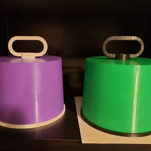 May include: Two 3D printed cylindrical objects with handles. The object on the left is purple and the object on the right is green.