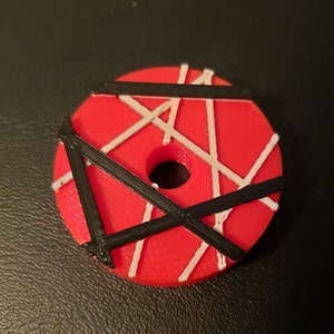 May include: Red, white, and black circular object with a hole in the center. The object has a geometric pattern of lines.