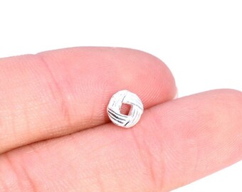 May include: A small, silver, circular charm with a woven design. The charm is held between two fingers.