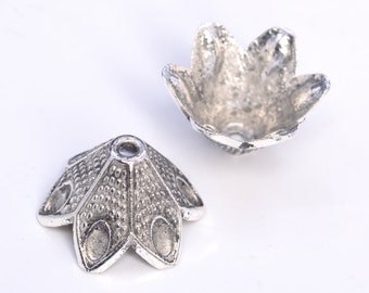 Op de afbeelding: Twee zilveren metalen bloemvormige kralencaps. De caps hebben een getextureerd oppervlak en een klein gaatje in het midden.