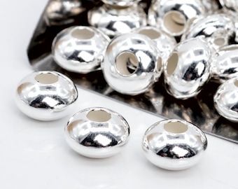 Può includere: Perle di metallo color argento con un grande foro al centro. Le perle sono rotonde e hanno una finitura liscia e lucida.