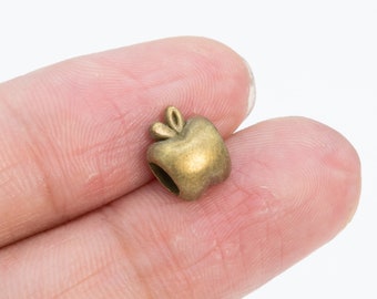 May include: A small, gold-colored metal charm shaped like an apple. The charm has a stem and leaf detail.