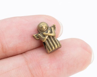 May include: A small, gold-colored metal angel figurine with wings and a smiling face. The angel is holding its hands together in front of its chest.