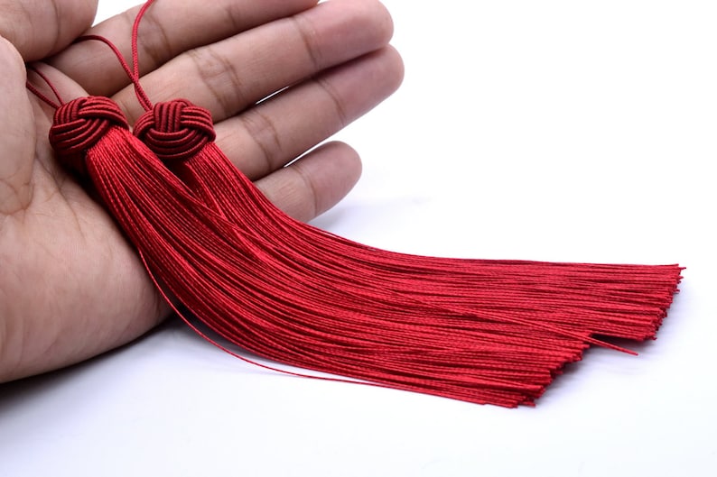 May include: Two red tassel ornaments with a knotted top. The tassels are made of thin strands of red thread and are about 10 inches long.