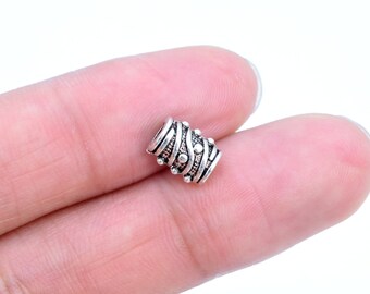 Pode incluir: Conta de metal prateada com um design decorativo de linhas onduladas e pequenos pontos. A conta mede aproximadamente 1 cm de comprimento.