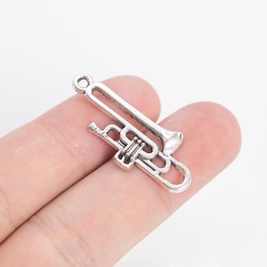 May include: A silver-coloured trombone charm. The charm is a miniature replica of the musical instrument, featuring a bell, slide, and tuning slide. The charm has a loop at the top for attaching to a necklace or bracelet. The trombone is a musical instrument.