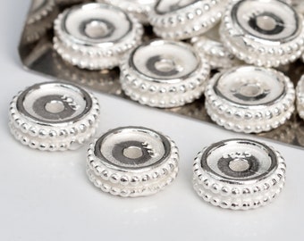 May include: Silver spacer beads with a round, flat design and a small hole in the centre. The beads have a textured edge with small, raised dots.