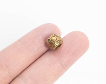 May include: A gold-colored metal bead with a hexagonal pattern. The bead is about the size of a dime.