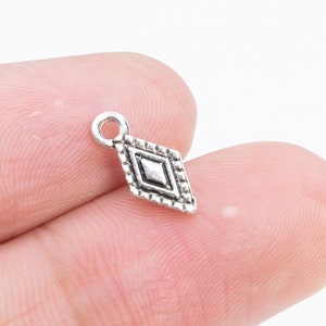 Puede incluir: Encanto de plata en forma de diamante con un borde texturizado. El encanto tiene un bucle en la parte superior para sujetarlo a un collar o pulsera.