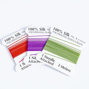 May include: Three spools of silk thread in red, purple, and green. Each spool is labeled "100% Silk" and "For Stringing Pearls." The green spool is 2 meters long and includes a needle. Ideal for jewelry making.