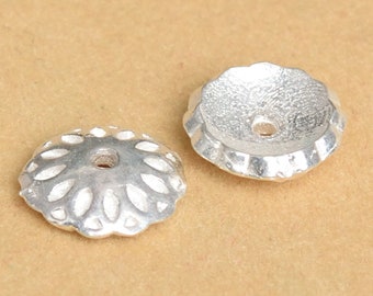 May include: Two silver-toned metal bead caps with a decorative design. The caps have a round shape with a hole in the center.