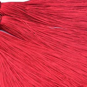 May include: Three red tassel trims with knotted tops. The tassels are made of thin, silky threads.