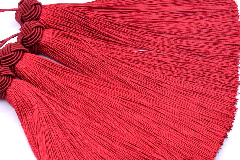 May include: Three red tassel trims with knotted tops. The tassels are made of thin, silky threads.