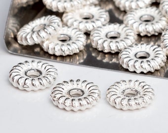 May include: Silver-toned metal beads with a decorative, twisted design. The beads have a circular shape with a hole in the center.