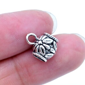 May include: Silver-toned metal cord end with a floral design. The cord end has a loop for attaching to a cord or chain.