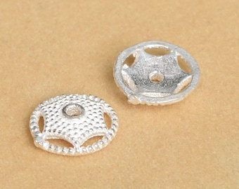 May include: Two silver-toned metal bead caps with a star-shaped design. The bead caps have a small hole in the center for threading.