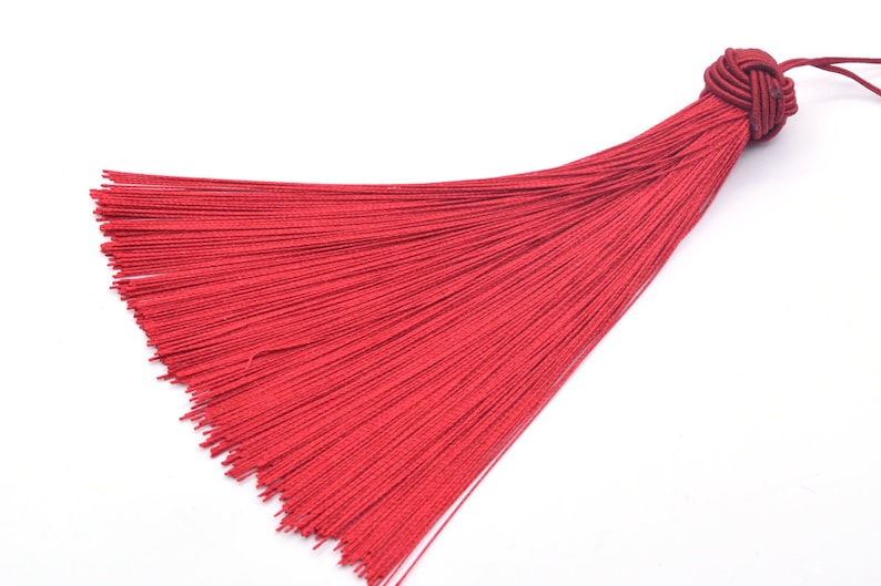 May include: A red tassel with a knotted top. The tassel is made of thin strands of fabric and is about 6 inches long.