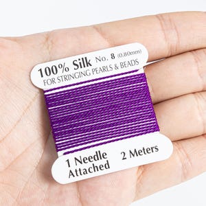 May include: A spool of purple 100% silk thread for stringing pearls and beads. The label reads "No. 8 (0.80mm)" and "2 Meters". It includes one needle attached. The thread is tightly wound on a white card.