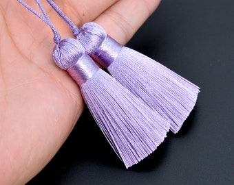 May include: Two lavender silk tassels with a knotted top. The tassels are soft and fluffy, and they would be perfect for adding a touch of elegance to any project.