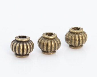 May include: Three antique bronze-colored beads with a ribbed, pumpkin-like design. Each bead has a small, cylindrical top and a rounded base. The beads are likely used for jewelry making or other crafts.