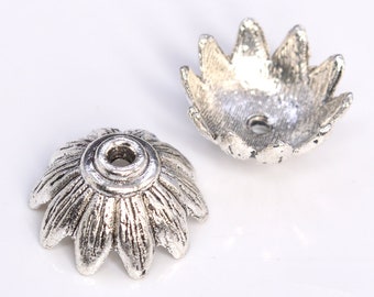 May include: Two silver metal flower-shaped bead caps with a hole in the center. The caps have a textured surface and are designed to be used as decorative accents for jewelry making.