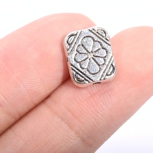 May include: Silver metal square bead with a decorative flower design.