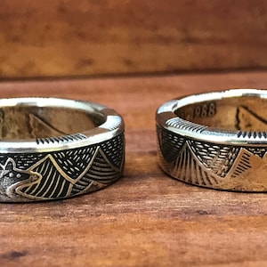 May include: Two silver rings made from a 1988 Canadian dollar coin. The rings feature a mountain range design with a wolf silhouette.