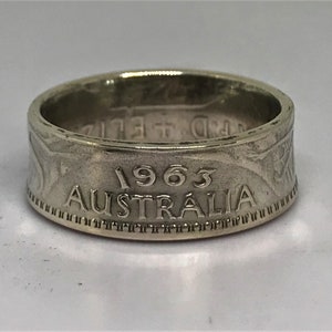 May include: A silver ring made from a 1963 Australian coin. The ring features the year "1963" and the word "AUSTRALIA" engraved on the band.