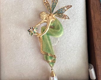 May include: A gold-toned fairy brooch with green enamel and a pearl drop. The fairy is sitting with wings outstretched and holding a flower.