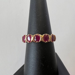 May include: A gold band ring with seven oval-shaped ruby gemstones set in a prong setting.
