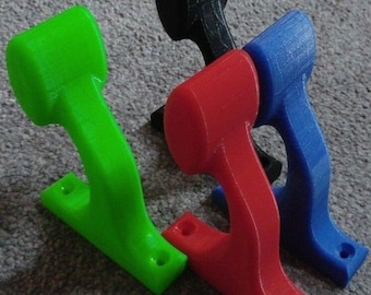 May include: Four 3D printed wall hooks in different colours: green, red, blue and black. The hooks are designed with a curved shape and have a flat base for mounting.