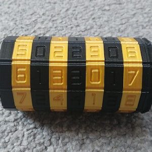 May include: A black and gold combination lock with the numbers 502290613017418. The lock is made of plastic and has a cylindrical shape.