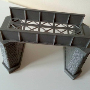 May include: A grey plastic model railway bridge with stone supports. The bridge has a lattice design and is designed for use with model railway sets.