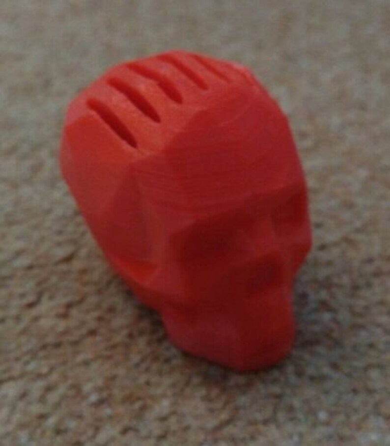 May include: A bright red, 3D printed skull with a geometric design. The skull has a textured surface and is missing the top of the head.